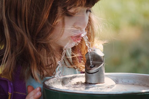 Child enjoying refreshing water from a drinking fountain outdoors.