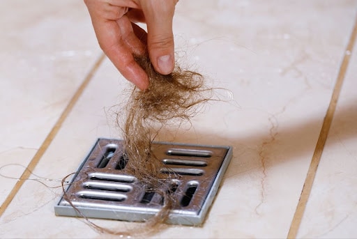 Removing hair from a drain to prevent clogs and maintain plumbing.