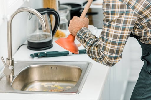 A plumber uses a plunger to clear a clogged kitchen sink effectively.