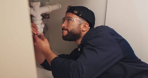 A plumber fixing a sink under the cabinet to prevent leaks and ensure proper drainage.