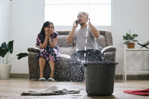 Water leak plumbing emergency causes panic, with a bucket collecting dripping water indoors.