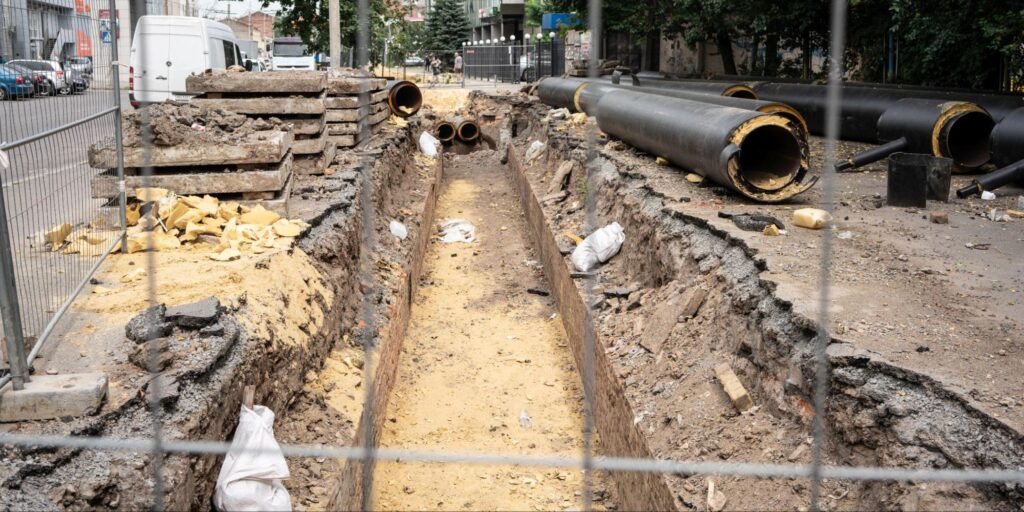 Construction site showing trench with pipes and excavation materials for utility installation.