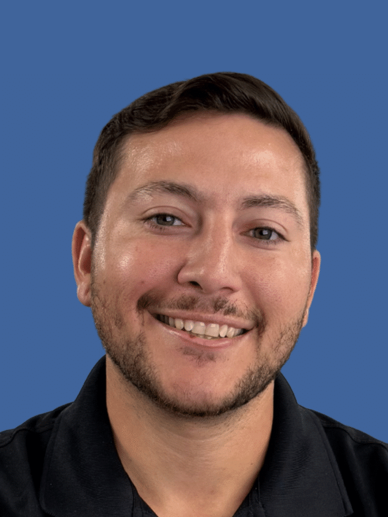Smiling man in a black shirt with a blue background.