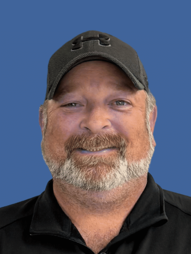 Smiling bearded man wearing a cap, showcasing a friendly demeanor against a blue background.