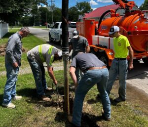 Workers repairing a utility line with a vacuum truck in a residential area.