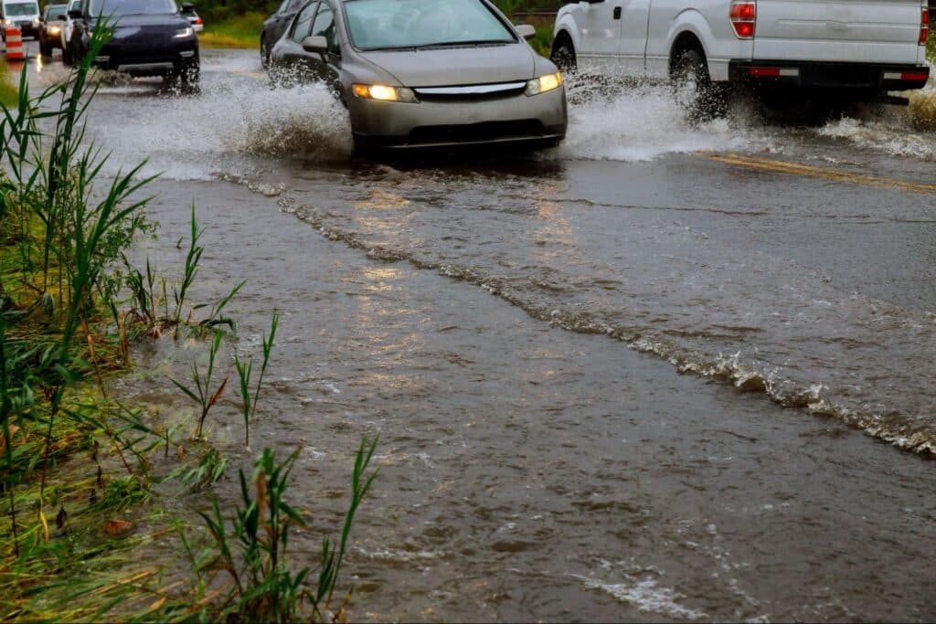 Cars navigate through flooded streets during heavy rain.