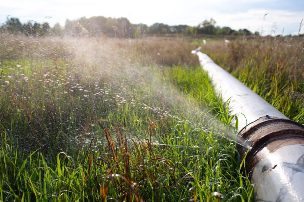 Irrigation system spraying water on lush green grass in a sunny landscape.