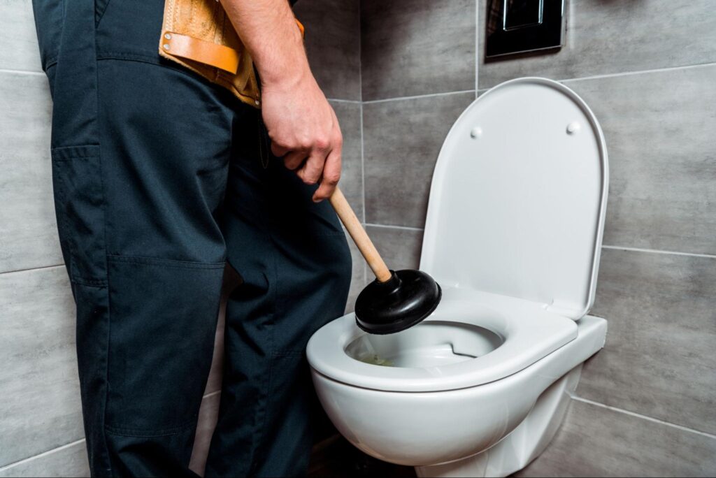 Plumber using a plunger to clear a clogged toilet in a modern bathroom.