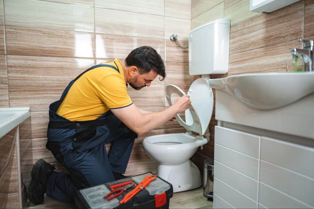 Plumber fixing a toilet clog in a modern bathroom with tools and focus.