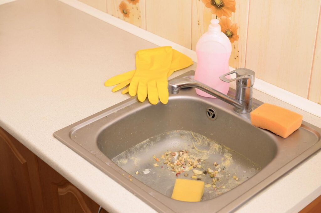 Cleaning supplies on a kitchen sink, featuring gloves, soap, and sponges.