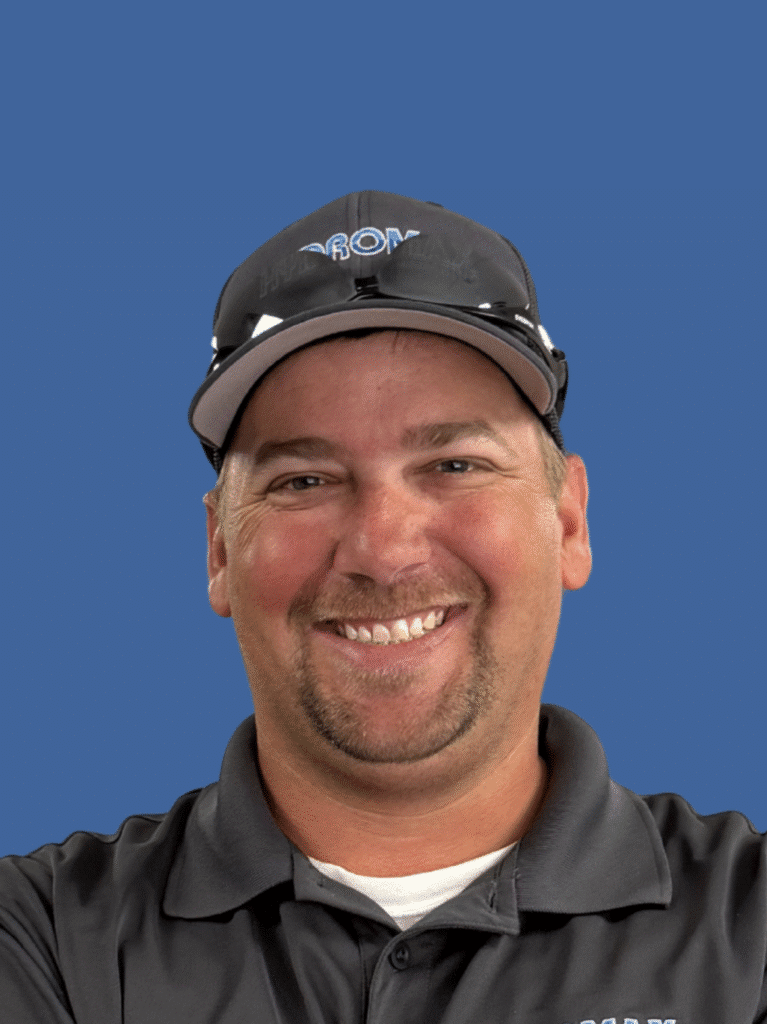 Smiling man in a gray shirt with a cap against a blue background.