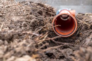 Close-up view of a pipe being installed in freshly dug soil.