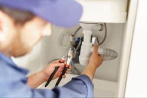 Plumber repairing a sink with tools under a kitchen cabinet.
