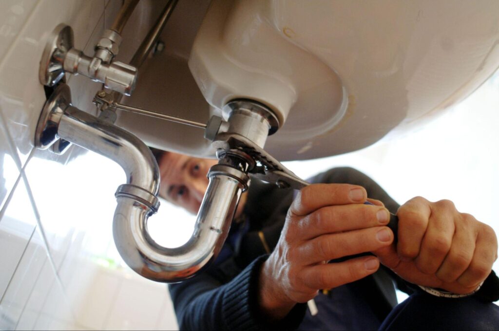 Plumber repairing sink pipes under the basin with a wrench conveying Plumbing Services