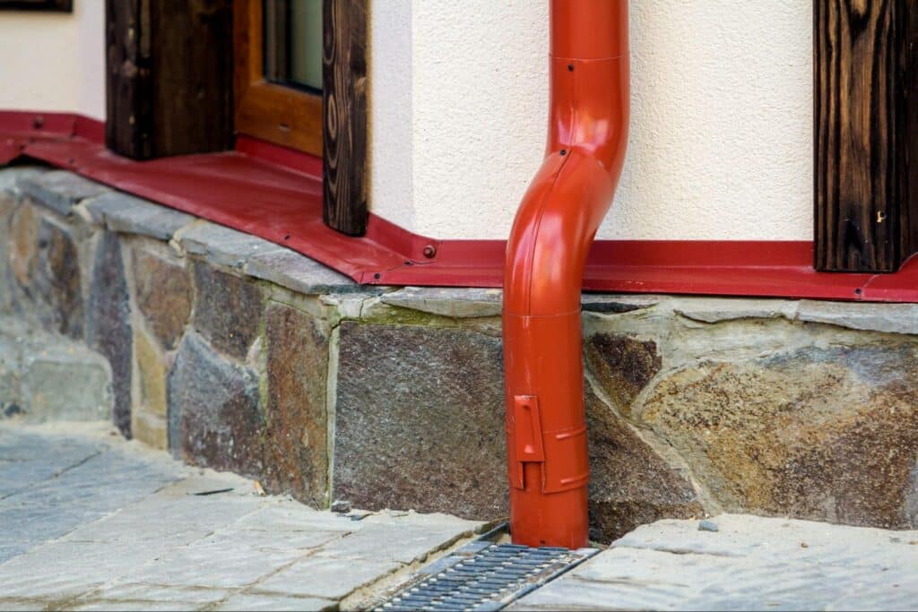 Red downspout directs rainwater away from a stone foundation for effective drainage.
