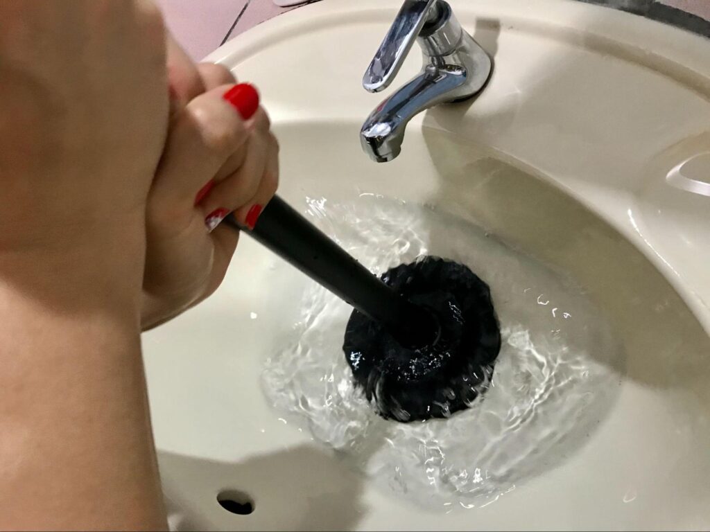 Person using a plunger to clear a clogged sink and restore proper drainage.