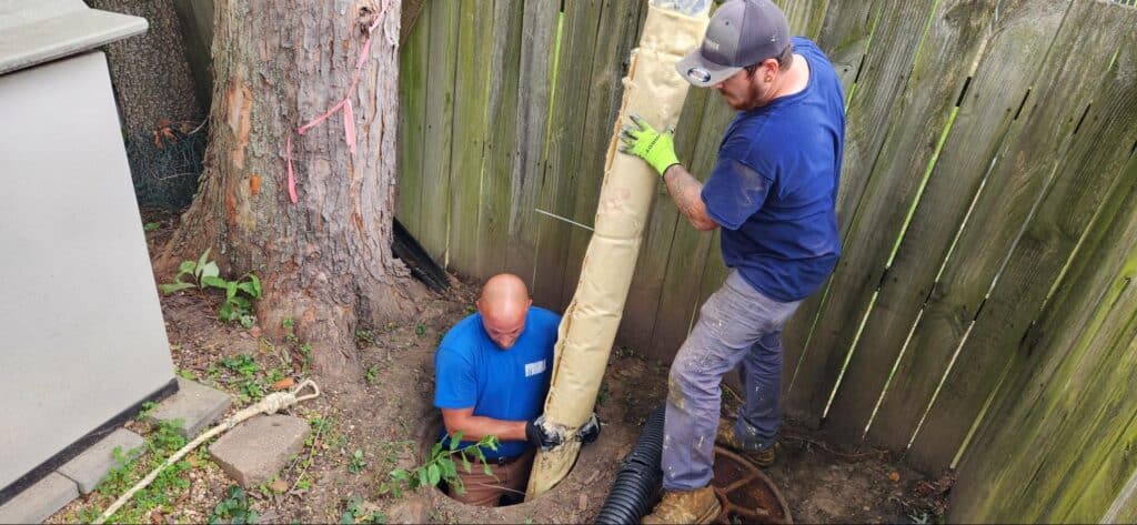 Professionals repairing a drainage system with a pipe in a residential yard.