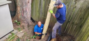 Professionals repairing a drainage system with a pipe in a residential yard.