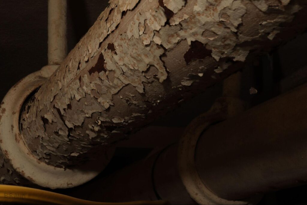 Rusty pipe with peeling paint in a dimly lit industrial setting.