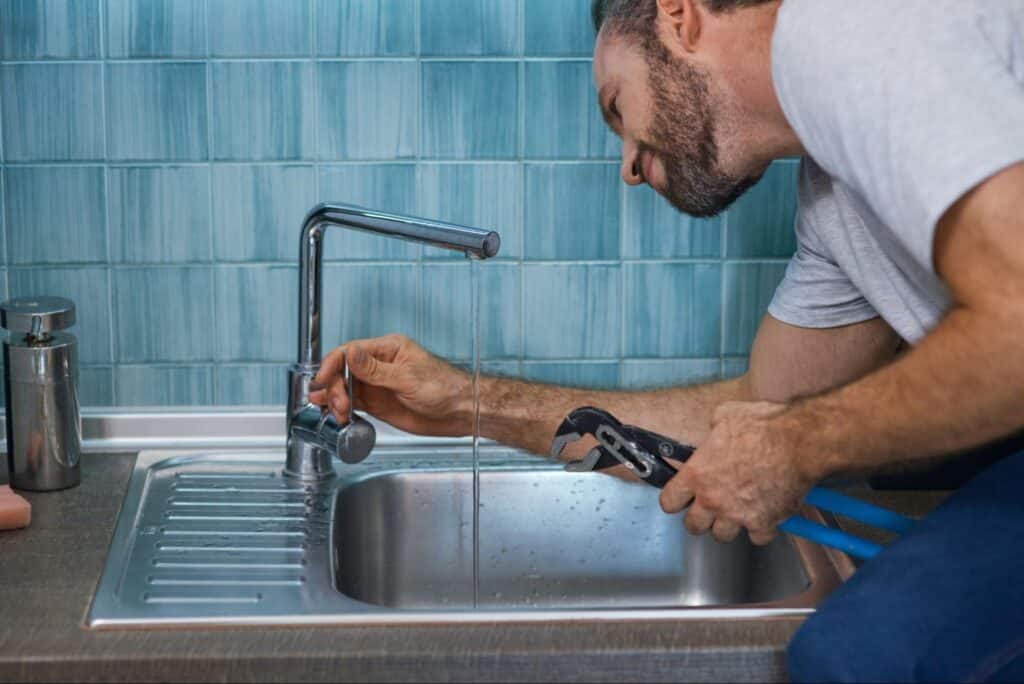 Man repairing a kitchen sink faucet with plumbing tools.