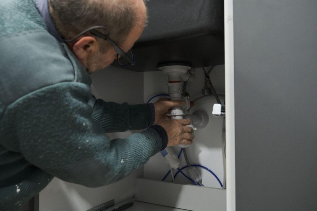 Plumber repairing a sink under the cabinet for efficient water drainage based on annual plumbing service contract.