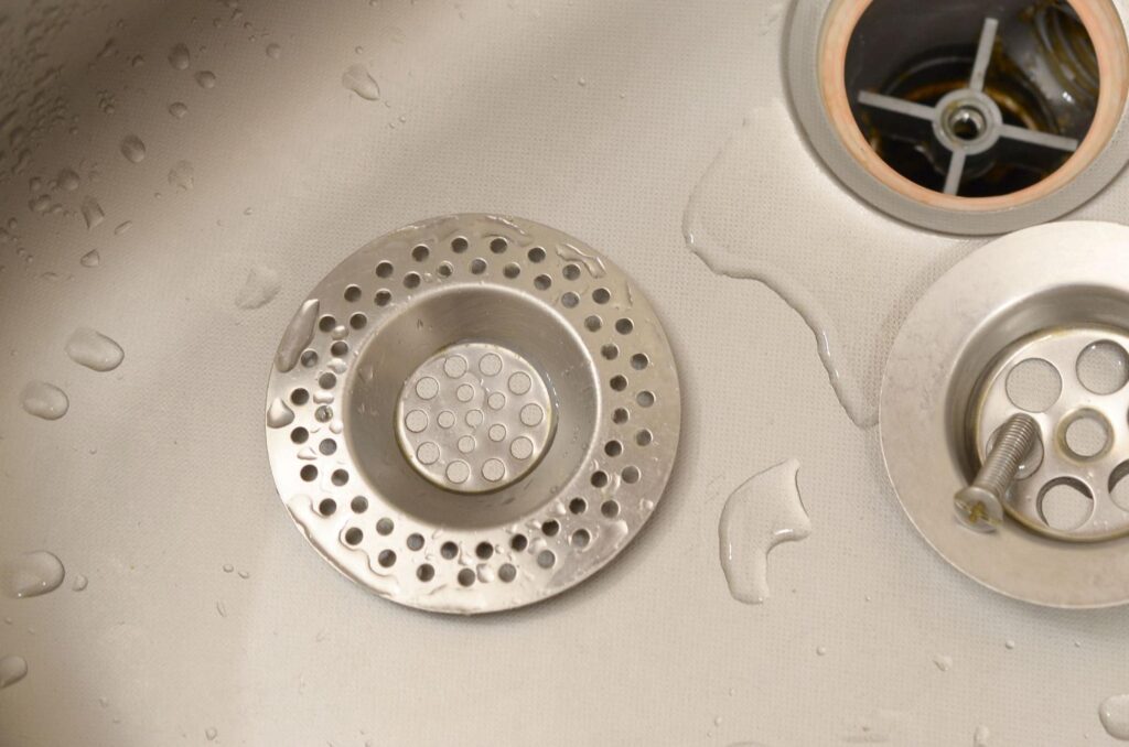 Stainless steel sink drain cover with water droplets and smooth finish. Recover Jewelry from a Drain concept