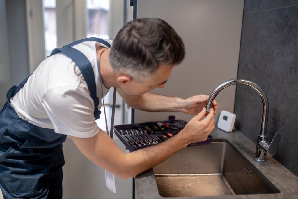Plumber repairing a kitchen sink faucet with professional tools.