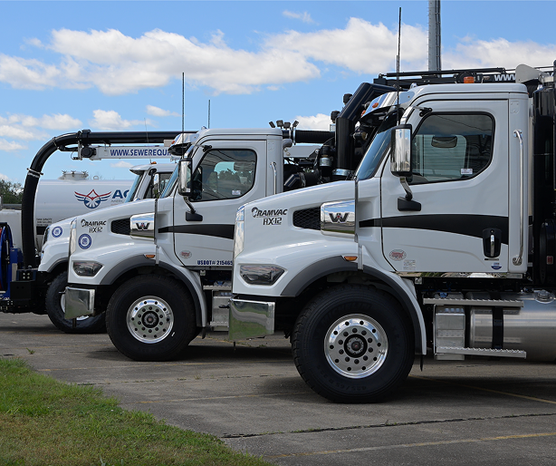Four white service trucks lined up on a sunny day with fluffy clouds. Trucks have various equipment like hoses, creating a professional and industrial tone.